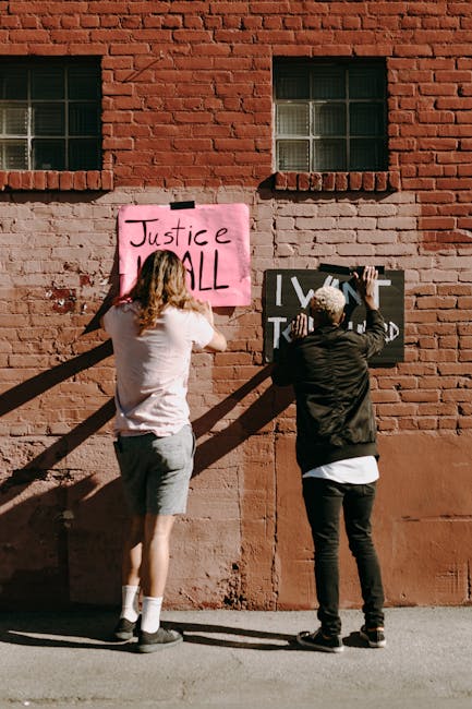 Two people hang protest signs on a brick wall, advocating for justice and equality.