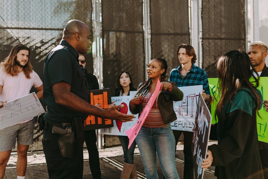 A diverse group of people engaged in a peaceful protest outdoors, discussing with a police officer.
