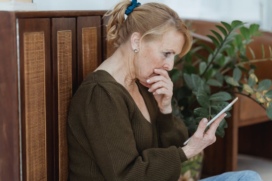 Senior woman deeply focused on her smartphone, indoors with plants and cozy decor.
