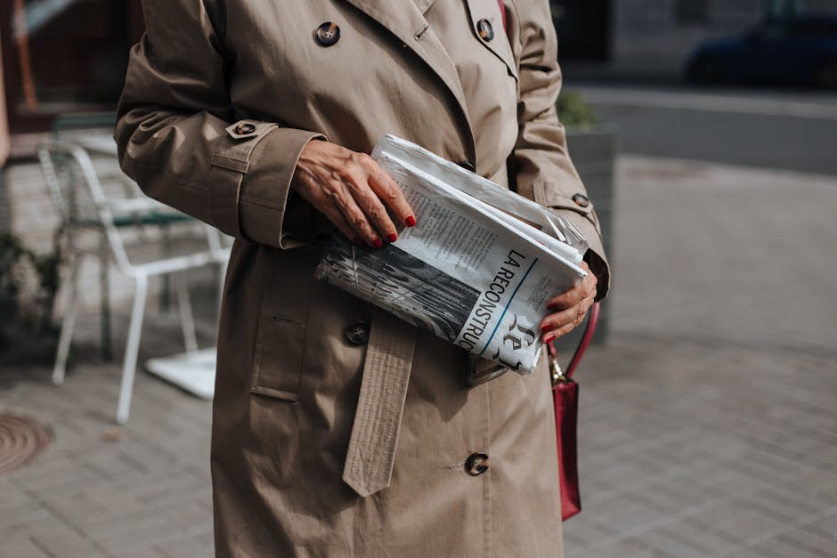 A woman in a trench coat holding a newspaper on a city street. Perfect for lifestyle and fashion themes.