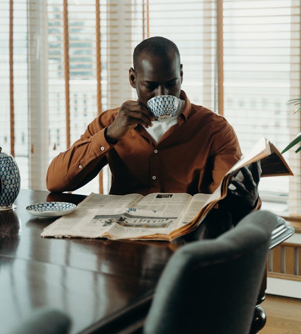 African American man enjoying coffee while reading newspaper indoors, in a relaxed setting.